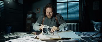 Movie still from “Max Payne” (2008), directed by John Moore – A man sitting at a table looking at a picture; Medium shot, High angle