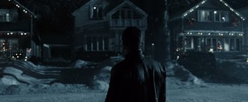 Movie still from “Max Payne” (2008), directed by John Moore – A man standing in front of a house at night; Wide shot, Over the shoulder angle
