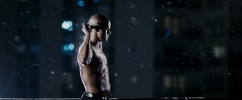 Movie still from “Max Payne” (2008), directed by John Moore – A bald man with no shirt is holding a cell phone in his ear; Medium shot, Low angle