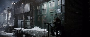 Movie still from “Max Payne” (2008), directed by John Moore – A man sitting on a bench in front of a building; Wide shot, High angle