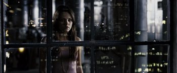 Movie still from “Max Payne” (2008), directed by John Moore – A woman standing in front of a window looking out at the city lights; Medium shot, High angle