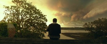 Movie still from “Max Steel” (2016), directed by Stewart Hendler – A man sitting on a ledge looking out over a body of water; Wide shot, Low angle