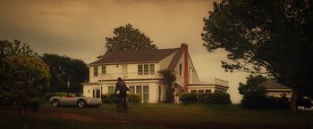 Movie still from “Max Steel” (2016), directed by Stewart Hendler – A person riding a bike in front of a house; Extreme Wide shot, Low angle