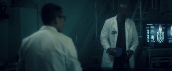 Movie still from “Max Steel” (2016), directed by Stewart Hendler – Two men in white lab coats are standing in front of a staircase; Medium shot, Over the shoulder angle