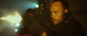 Movie still from “Max Steel” (2016), directed by Stewart Hendler – A man holding a gun while wearing gloves and a black shirt; Close Up shot, Low angle