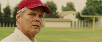 Movie still from “McFarland, USA” (2015), directed by Niki Caro – An older man wearing a baseball cap stares into the distance; Close Up shot, Over the shoulder angle