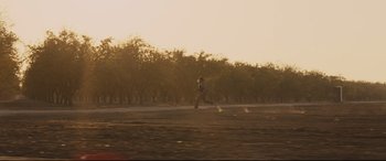 Movie still from “McFarland, USA” (2015), directed by Niki Caro – A person running in a field with trees in the background; Extreme Wide shot, Low angle