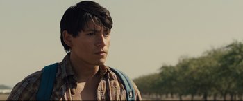 Movie still from “McFarland, USA” (2015), directed by Niki Caro – A young man with a backpack is standing in the grass; Close Up shot, Over the shoulder angle