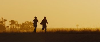 Movie still from “McFarland, USA” (2015), directed by Niki Caro – Two people running on a dirt road at sunset; Extreme Wide shot, Low angle