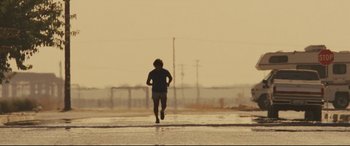 Movie still from “McFarland, USA” (2015), directed by Niki Caro – A man running on a wet road in the middle of the day; Wide shot, Low angle