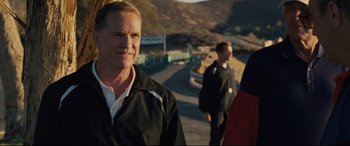 Movie still from “McFarland, USA” (2015), directed by Niki Caro – A man standing next to another man on a race track; Close Up shot, Over the shoulder angle