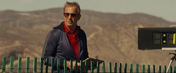 Movie still from “McFarland, USA” (2015), directed by Niki Caro – A man standing in front of a green fence; Medium shot, Low angle