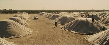 Movie still from “McFarland, USA” (2015), directed by Niki Caro – A man standing on a dirt road next to a truck; Extreme Wide shot, High angle