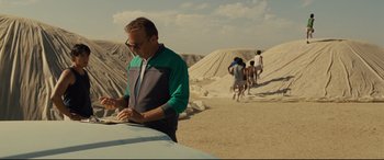 Movie still from “McFarland, USA” (2015), directed by Niki Caro – A man writing on a piece of paper in the desert; Medium shot, Over the shoulder angle