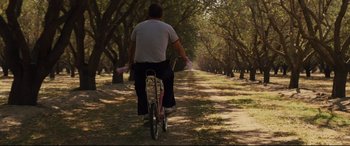 Movie still from “McFarland, USA” (2015), directed by Niki Caro – A man riding a bike down a dirt road; Wide shot, Low angle