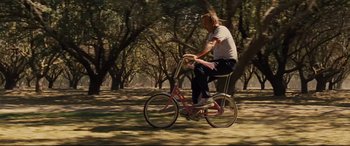 Movie still from “McFarland, USA” (2015), directed by Niki Caro – A man is riding a pink bike in a park; Wide shot, High angle