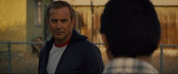 Movie still from “McFarland, USA” (2015), directed by Niki Caro – A man standing next to another man in front of a fence; Close Up shot, Over the shoulder angle