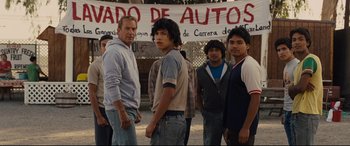 Movie still from “McFarland, USA” (2015), directed by Niki Caro – A group of men standing next to each other in a parking lot; Medium shot, Low angle