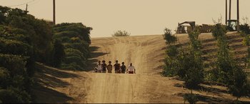 Movie still from “McFarland, USA” (2015), directed by Niki Caro – A group of people sitting on top of a dirt road; Extreme Wide shot, High angle