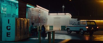 Movie still from “McFarland, USA” (2015), directed by Niki Caro – Two people sitting on a bench in front of a building; Wide shot, Over the shoulder angle