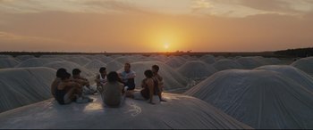 Movie still from “McFarland, USA” (2015), directed by Niki Caro – A group of people sitting on top of a sandy beach; Wide shot, High angle