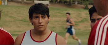 Movie still from “McFarland, USA” (2015), directed by Niki Caro – A man in a white shirt is looking at the camera while a man in a red and white shirt is running behind him; Close Up shot, Over the shoulder angle