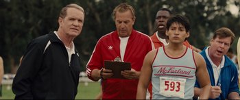 Movie still from “McFarland, USA” (2015), directed by Niki Caro – A group of men standing next to each other on top of a field; Medium shot, Over the shoulder angle