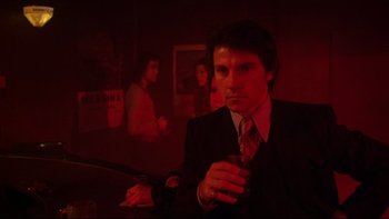 Movie still from “Mean Streets” (1973), directed by Martin Scorsese – A man sitting at a table with a drink in his hand; Medium shot, Low angle