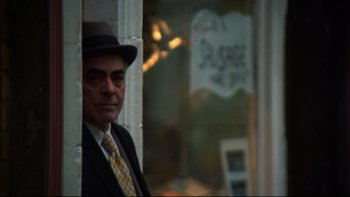 Movie still from “Mean Streets” (1973), directed by Martin Scorsese – A man in a suit and tie standing in front of a store window; Medium shot, Over the shoulder angle