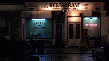 Movie still from “Mean Streets” (1973), directed by Martin Scorsese – A man walking down the sidewalk in front of a restaurant; Wide shot, High angle