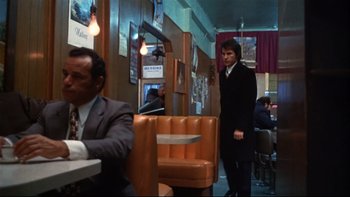 Movie still from “Mean Streets” (1973), directed by Martin Scorsese – A man in a suit and tie standing in a restaurant; Wide shot, Over the shoulder angle