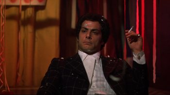 Movie still from “Mean Streets” (1973), directed by Martin Scorsese – A man in a black and white suit is sitting down; Medium shot, Low angle
