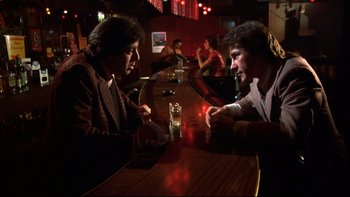 Movie still from “Mean Streets” (1973), directed by Martin Scorsese – Two men are sitting at a bar and one of them has a drink in his hand; Medium shot, Low angle