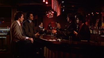 Movie still from “Mean Streets” (1973), directed by Martin Scorsese – A group of men sitting at a bar talking to each other; Wide shot, Low angle