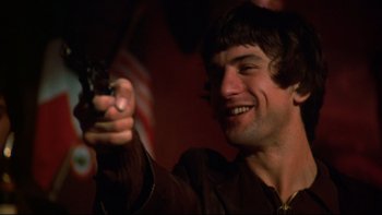 Movie still from “Mean Streets” (1973), directed by Martin Scorsese – A young man holding a gun and smiling for the camera; Close Up shot, Low angle