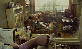 Movie still from “Meantime” (1983), directed by Mike Leigh – A group of people sitting in a living room next to each other; Wide shot, High angle