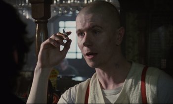 Movie still from “Meantime” (1983), directed by Mike Leigh – A bald man smoking a cigarette in a room; Close Up shot, Over the shoulder angle