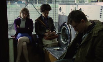 Movie still from “Meantime” (1983), directed by Mike Leigh – Three people sitting on a bus looking at something on the floor; Medium shot, Low angle