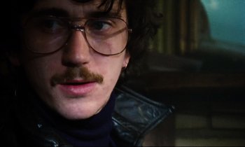Movie still from “Meantime” (1983), directed by Mike Leigh – A person wearing glasses and a leather jacket; Close Up shot, Low angle