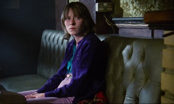 Movie still from “Meantime” (1983), directed by Mike Leigh – A woman sitting on a couch in front of a radio; Medium shot, Low angle