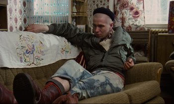 Movie still from “Meantime” (1983), directed by Mike Leigh – A man sitting on a couch with a hat on his head; Medium shot, High angle