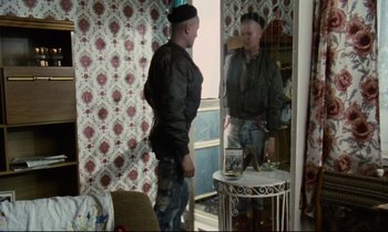 Movie still from “Meantime” (1983), directed by Mike Leigh – A man standing in front of a mirror in a room; Medium shot, Over the shoulder angle