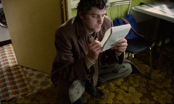 Movie still from “Meantime” (1983), directed by Mike Leigh – A man sitting on the ground reading a paper; Medium shot, High angle