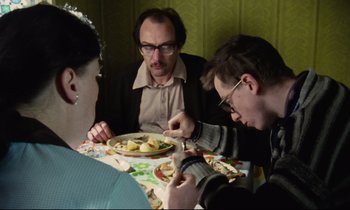Movie still from “Meantime” (1983), directed by Mike Leigh – A group of people sitting at a table eating food; Medium shot, Over the shoulder angle