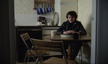Movie still from “Meantime” (1983), directed by Mike Leigh – A man sitting at a table with a cup of coffee; Medium shot, Low angle