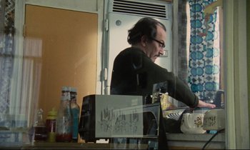 Movie still from “Meantime” (1983), directed by Mike Leigh – A man in a black shirt is cooking in a kitchen; Medium shot, Low angle