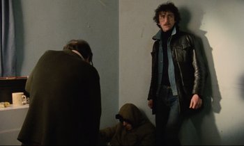 Movie still from “Meantime” (1983), directed by Mike Leigh – A group of people standing around a room; Medium shot, Low angle