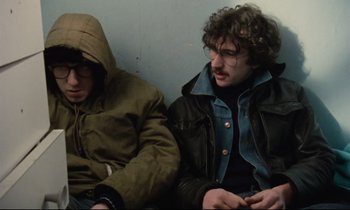 Movie still from “Meantime” (1983), directed by Mike Leigh – Two men sitting next to each other on a bench; Medium shot, Low angle