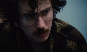 Movie still from “Meantime” (1983), directed by Mike Leigh – A man with a mustache and glasses looking at the camera; Close Up shot, Low angle