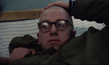 Movie still from “Meantime” (1983), directed by Mike Leigh – A bald man with glasses is holding a wooden stick; Close Up shot, High angle